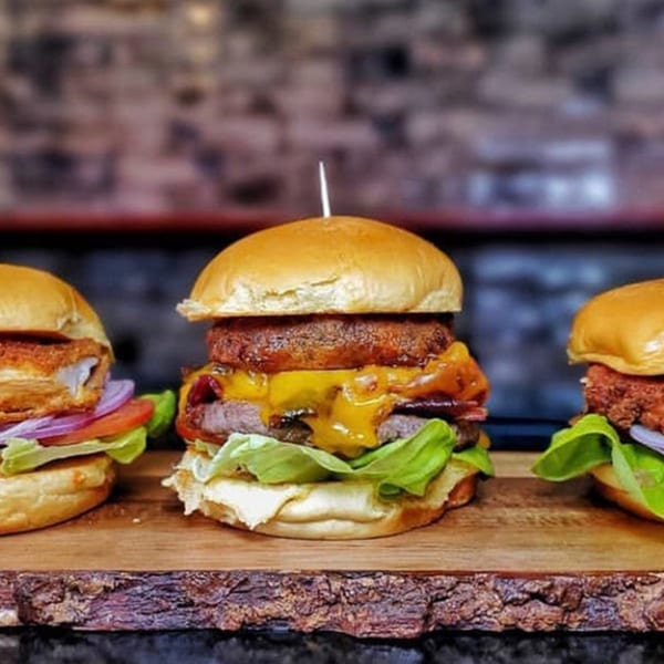Three Halalbee's burgers on a wooden board, with the center burger featuring a large onion ring.