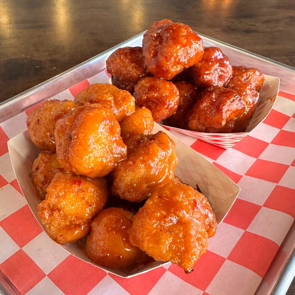 Two servings of Halalbee's sweet and spicy boneless wings in checkered paper boats on a tray.