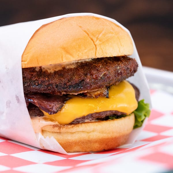 A Halalbee's double cheeseburger with bacon, lettuce, and sauce, wrapped in paper on a red checkered liner.