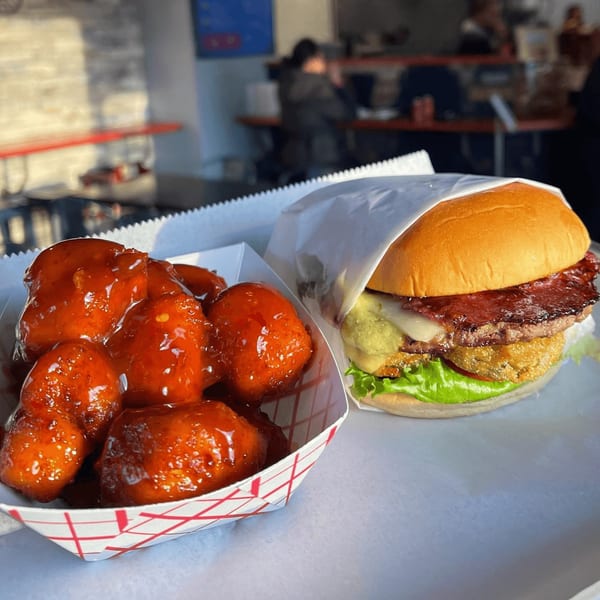 Halalbee's burger with bacon, cheese, and fried green tomato, alongside saucy boneless wings.