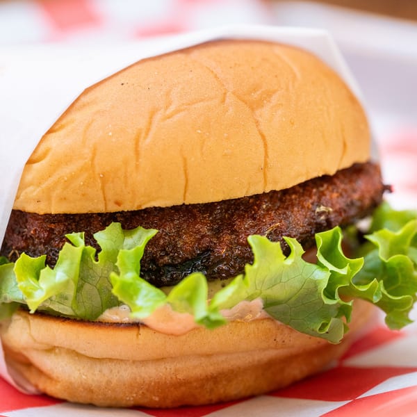A Halalbee's burger with a dark patty, fresh lettuce, and sauce on a bun.