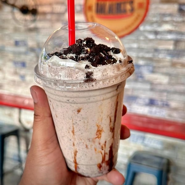 Hand holding a Halalbee's cookies and cream milkshake with whipped cream and cookie crumbles.