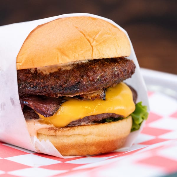 Halalbee's double cheeseburger with melted cheese, sauce, and lettuce, wrapped in paper on a checkered tray.